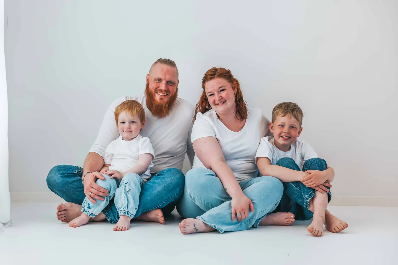 En glad familie på fire, der smiler til fotografen – taget af Amalie Sandgaard Photography.